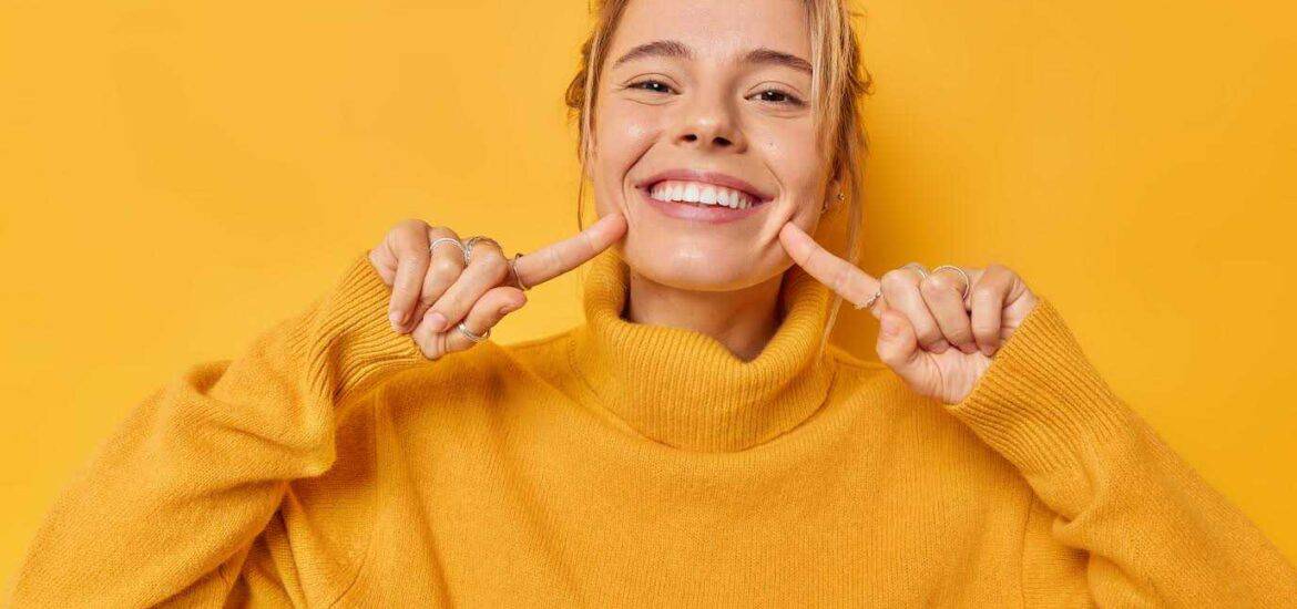 Young Girl Showing her Teeth with Pointing Finger in Yellow Background | Smile Virtual